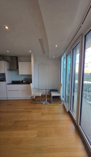 A modern kitchen with white cabinets, a central island, and a dining area with two chairs. - Luxury Canary Wharf Skyline Apartment (London)