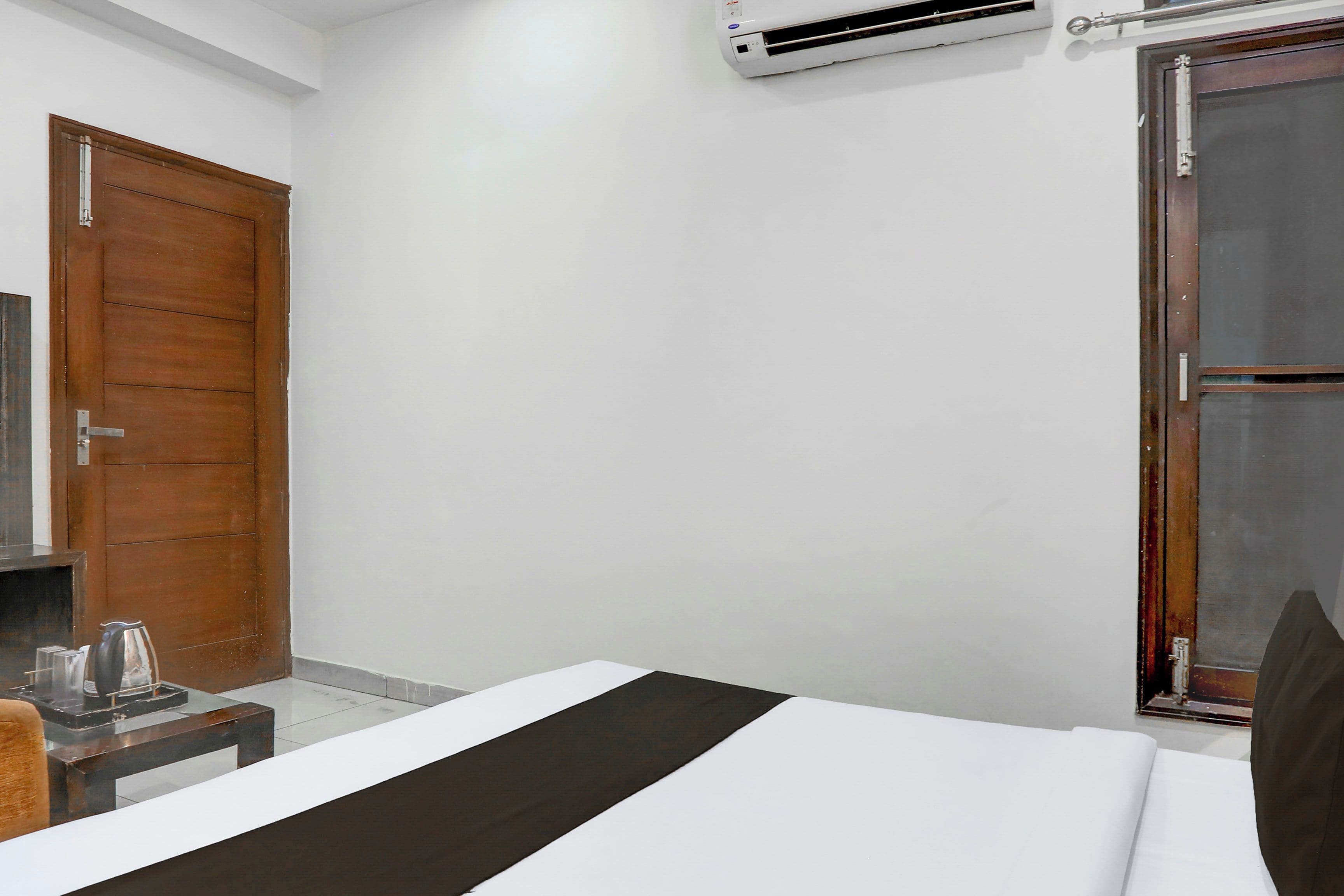 Habitación de hotel con cama, una puerta de madera, una mesita con hervidor y ventana con vistas.