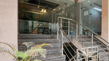Un escalier avec des rampes en métal menant à un niveau supérieur, entouré de murs de verre et agrémenté d’une plante en pot.