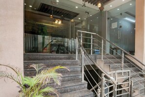 Eine Treppe mit Metallgeländern führt zu einer oberen Ebene, umgeben von Glaswänden und einem Blumentopf.