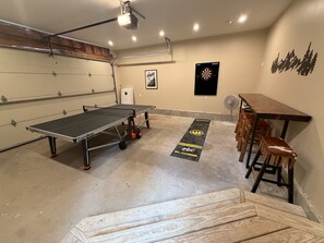 A ping pong table with a dartboard and chairs, a projector, and a wooden table with stools. - Tranquil 3-bedroom house with AC in charming Conway (Conway)