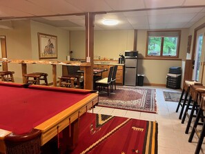 Ein Billardtisch mit Stühlen, ein Essbereich mit Stühlen und Tisch, eine Küche mit Geräten und ein Fenster mit Aussicht.