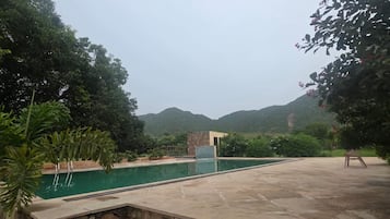 Una piscina con solárium de piedra y escalones que bajan a ella, rodeada de vegetación y colinas al fondo.