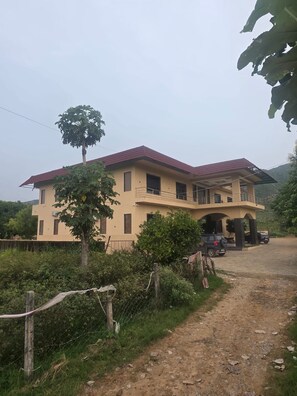 A two-story house with a balcony, a dirt driveway, and a tree in the foreground. - Aura Hills Pushkar By Kaya Hospitality (Pushkar)