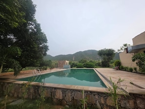 A rectangular pool with stone edging, surrounded by greenery and a view of hills.