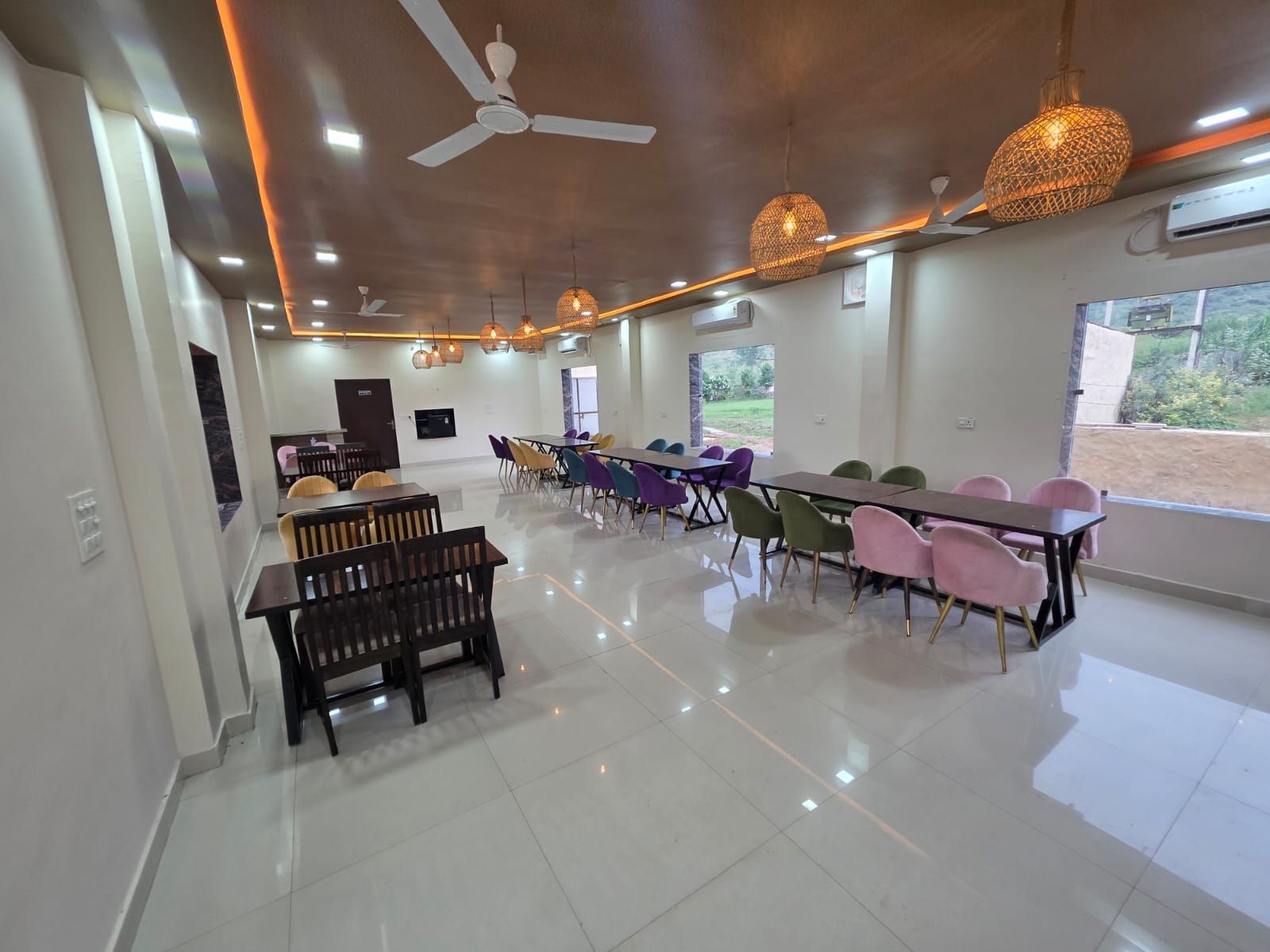A spacious dining area with multiple tables and chairs, ceiling fans, and pendant lighting.
