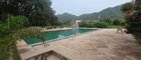 A swimming pool with a stone deck, surrounded by greenery and a mountain backdrop.