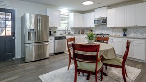 Una cocina moderna con armarios blancos, electrodomésticos de acero inoxidable, una mesa de comedor con sillas y una planta en maceta.