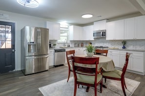 A modern kitchen with white cabinetry, stainless steel appliances, a dining table with chairs, and a potted plant. - Recently Remodeled Dtwn Frisco Home w/ Yard! (Frisco)