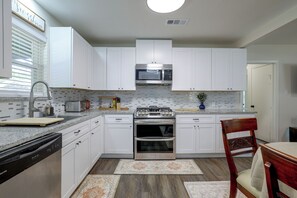 Una cocina moderna con armarios blancos, estufa de acero inoxidable, microondas y lavavajillas.