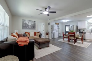 A modern living room with a sectional sofa, a dining area with a wooden table and chairs, a kitchen with white cabinets, and a ceiling fan. - Recently Remodeled Dtwn Frisco Home w/ Yard! (Frisco)