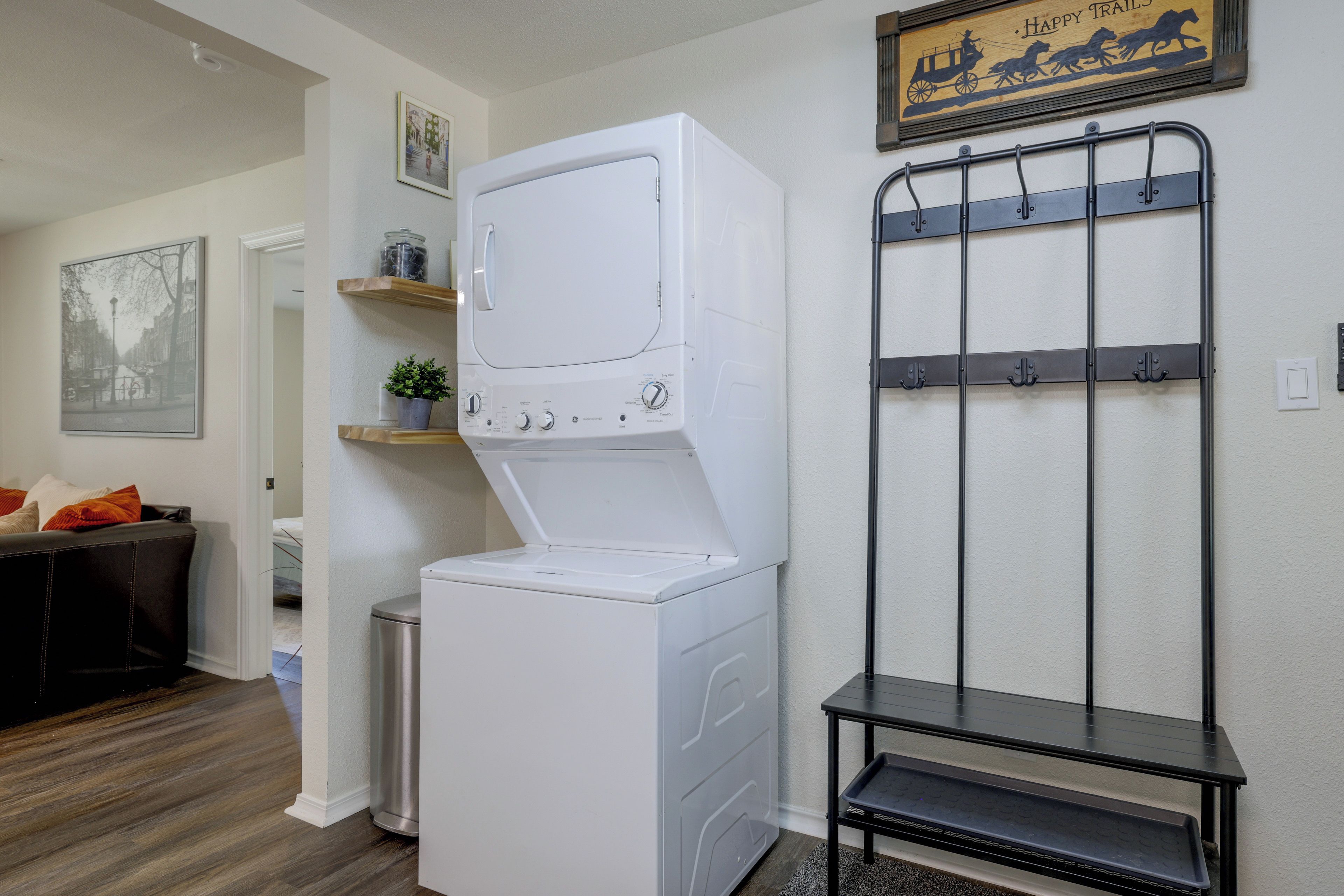 A laundry area with a front-loading washer and dryer, a metal drying rack, and a small table with a tray.