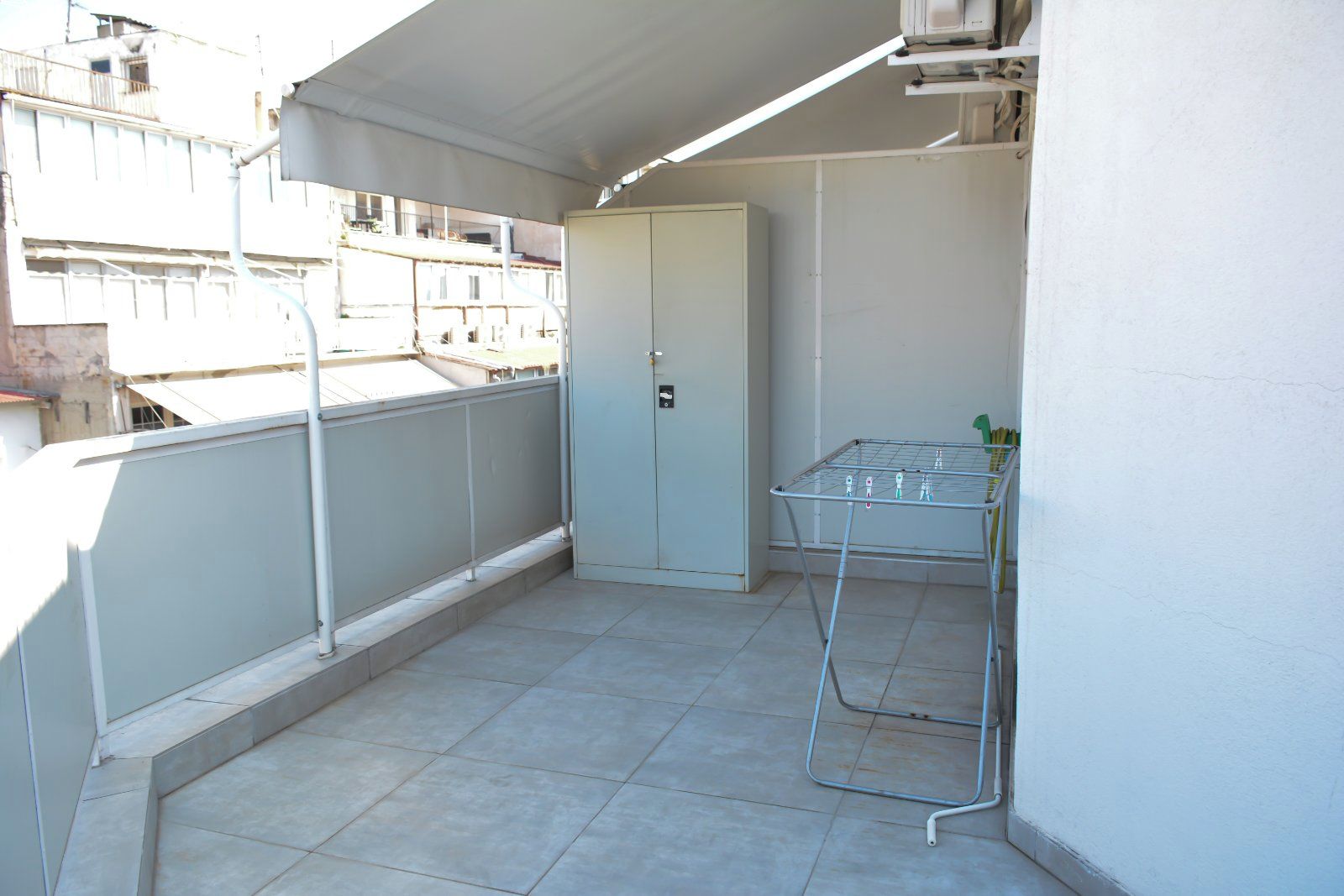 Varanda com varal de metal, uma porta branca e chão de azulejos.