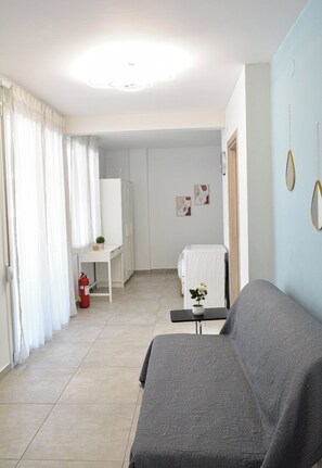 A living room with a grey sofa, a small table with a vase, a white radiator, and a door leading to another room. - Comfortable Central Studios with City Views in Thessaloniki (Thessaloniki)