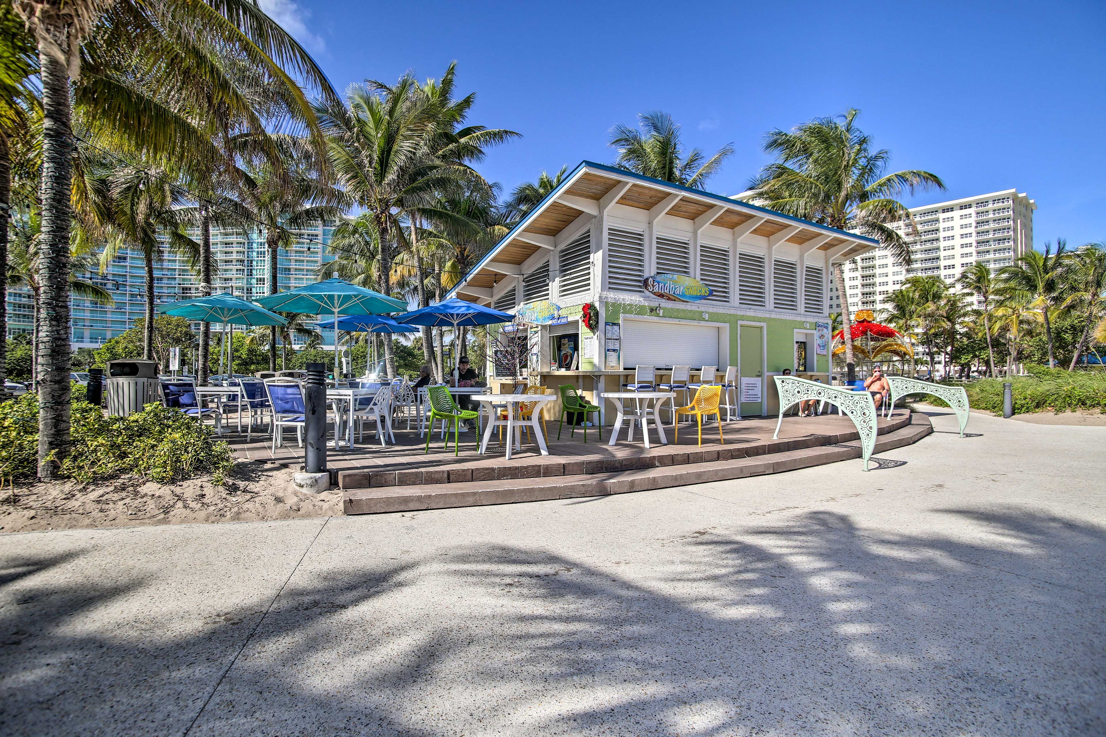 Un restaurante frente a la playa con terraza, palmeras y vista al océano.