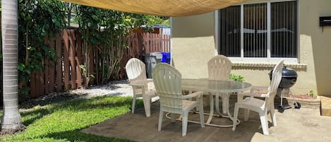 A patio with a table and chairs, a barbecue grill, and a shaded area.