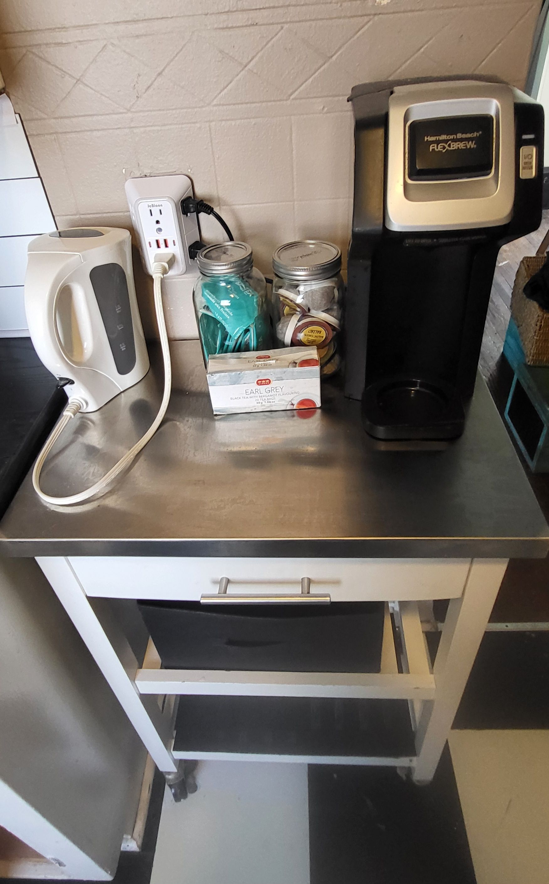 A kitchen counter with a coffee maker, a kettle, jars, and a box of Earl Grey tea.
