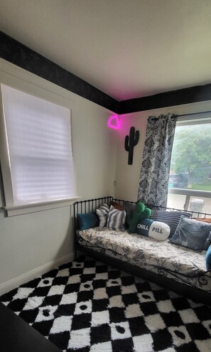 A corner room with a black and white checkered floor, a bed with pillows, a cactus decoration, and a window with a view.