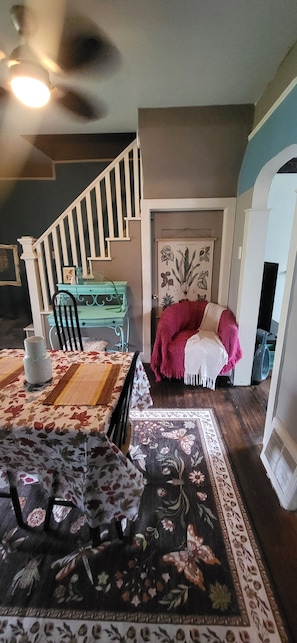 A dining area with a table set for two, a staircase, and a door with a botanical print.