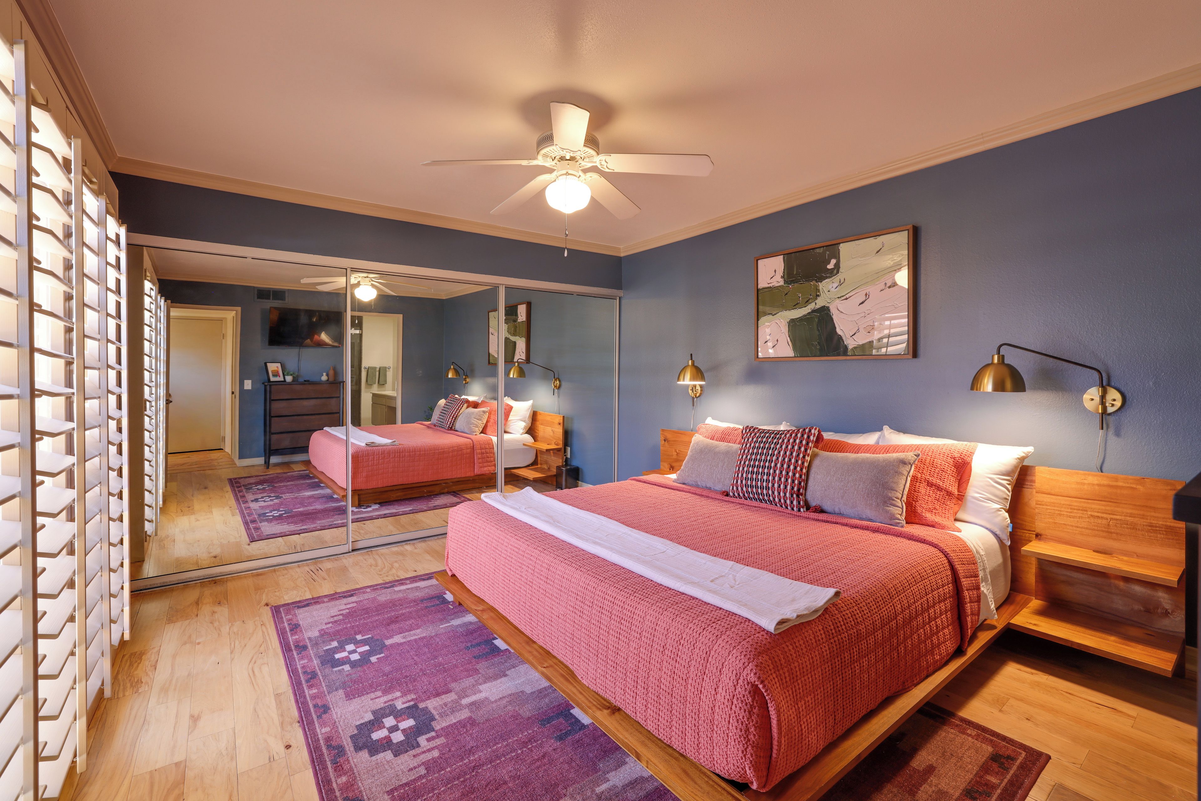 A bedroom with a large bed, a ceiling fan, a mirror, and a painting on the wall.