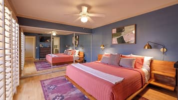 A bedroom with a large bed, a ceiling fan, a mirror, and a painting on the wall.