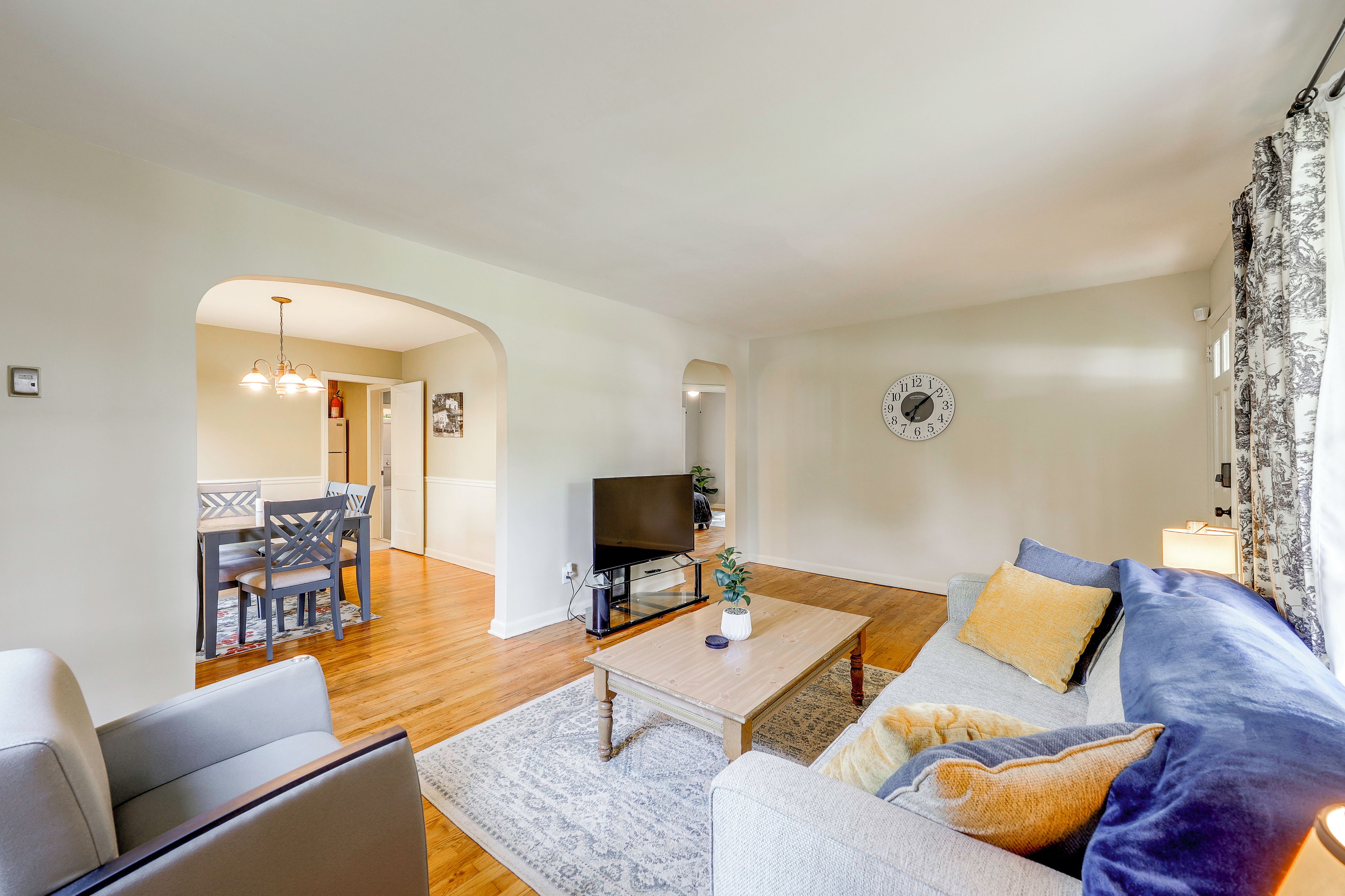 A living room with a sofa, a coffee table, and a TV. There is a dining area with chairs and a table.