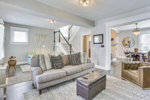 A spacious living room with a grey sofa, a brown ottoman, and a dining area with a wooden table and chairs.