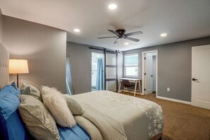 A bedroom with a bed, a desk, a ceiling fan, and a window.