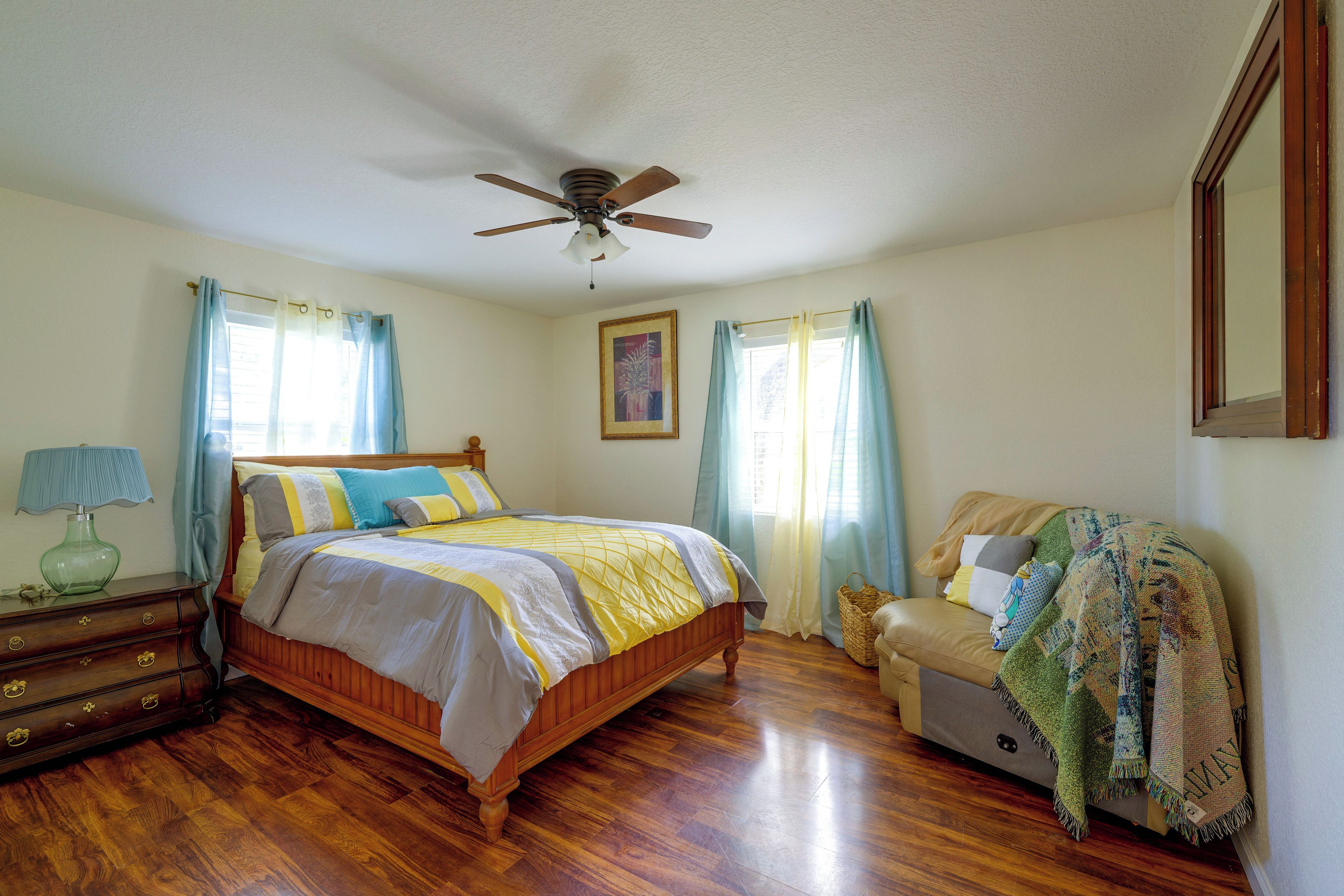 A bedroom with a wooden bed, a nightstand, a lamp, a ceiling fan, and a window with curtains.
