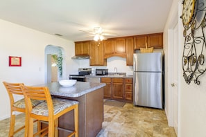 A kitchen with wooden cabinets, a stainless steel refrigerator, a microwave, and a dining area with a chair and a bowl. - Walk to Dining: Relax at 609 Gray (Wildwood)