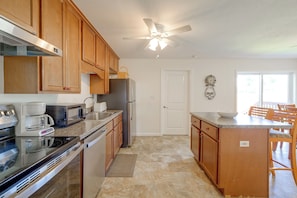A kitchen with wooden cabinets, a refrigerator, a microwave, a coffee maker, a sink, and a dining area with chairs and a table. - Walk to Dining: Relax at 609 Gray (Wildwood)