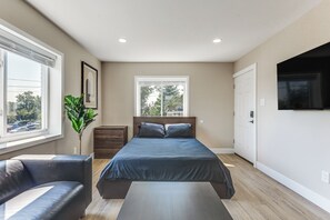 Ein Schlafzimmer mit einem Bett, einem Sessel, einer Kommode, einer Pflanze und einem Fernseher.
