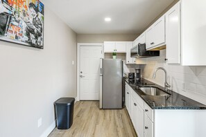 Eine moderne Küche mit weißen Schränken, einem Edelstahlkühlschrank, einer schwarzen Mülltonne und einer Arbeitsplatte mit Spüle und Toaster.