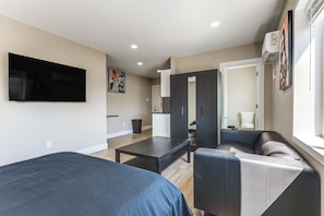 Ein modernes Hotelzimmer mit einem Flachbildfernseher, einer Couch, einem Tisch und einem Kleiderschrank.