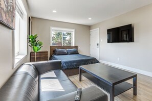 Ein modernes Schlafzimmer mit einem Bett, einem Sofa, einem Couchtisch, einem Fernseher und einem Fenster mit Blick ins Freie.