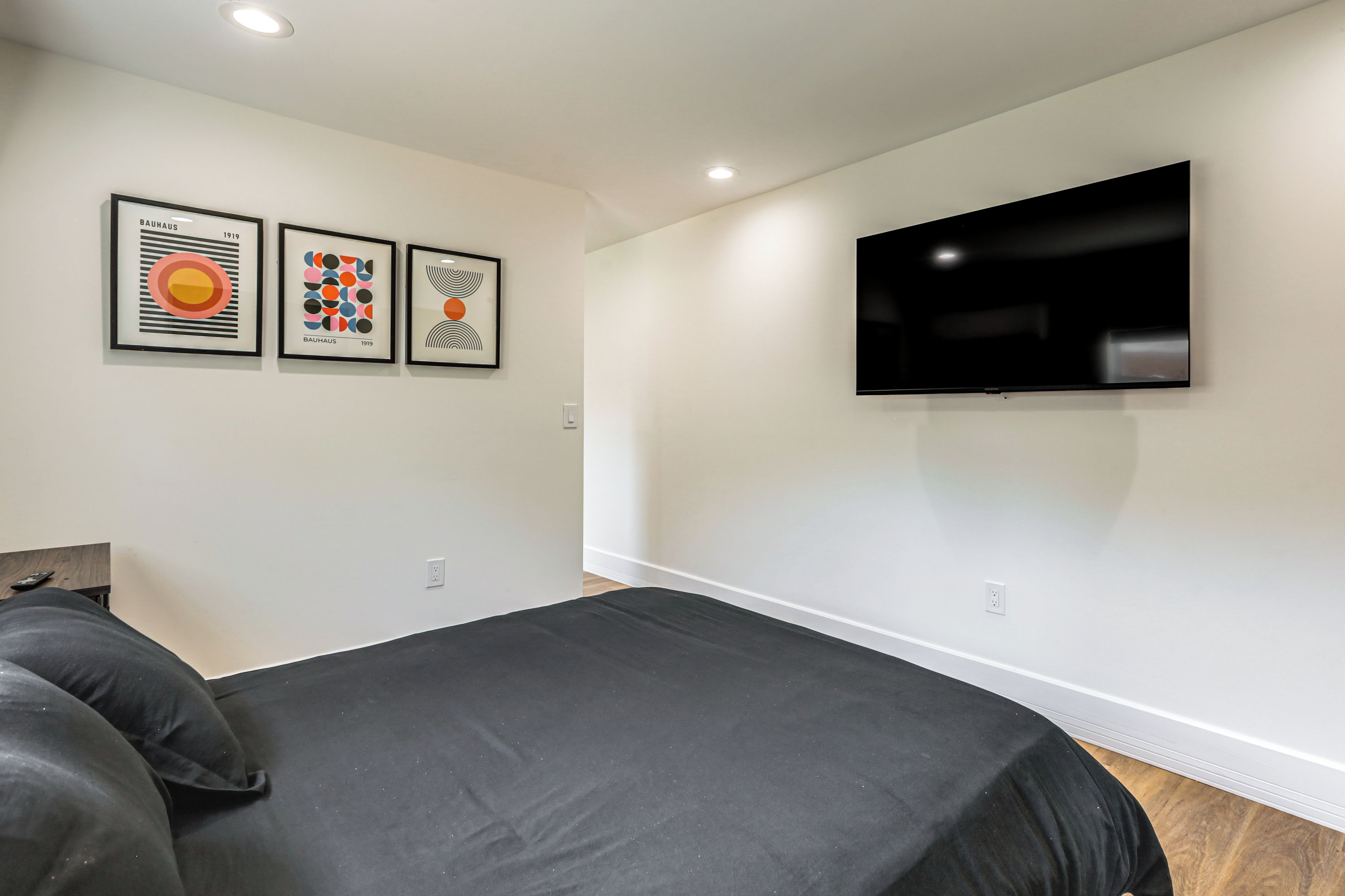 A bedroom with a bed, a flat-screen TV mounted on the wall, and three framed artworks on the wall.