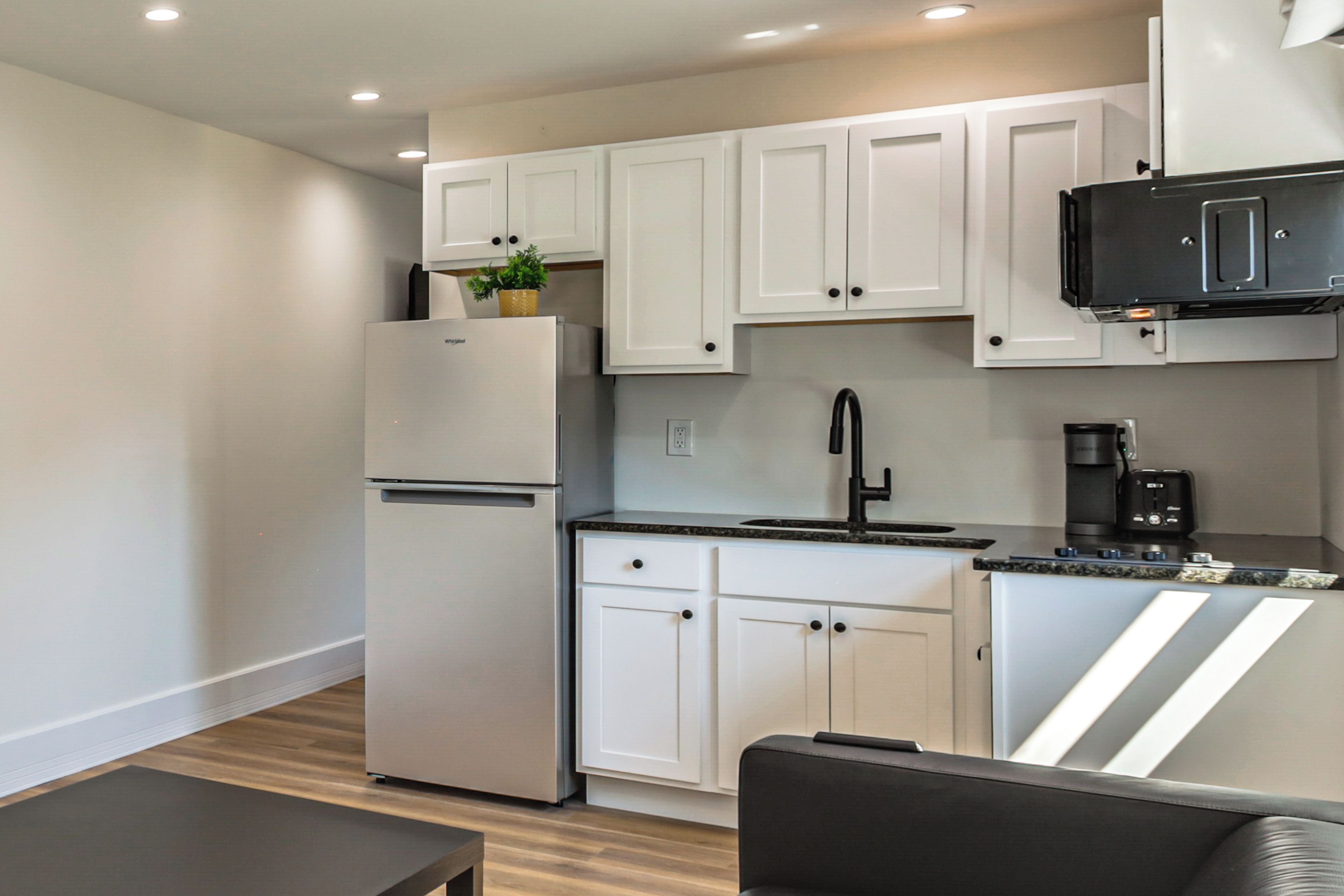 A modern kitchen with white cabinets, a stainless steel refrigerator, a coffee maker, and a black microwave.