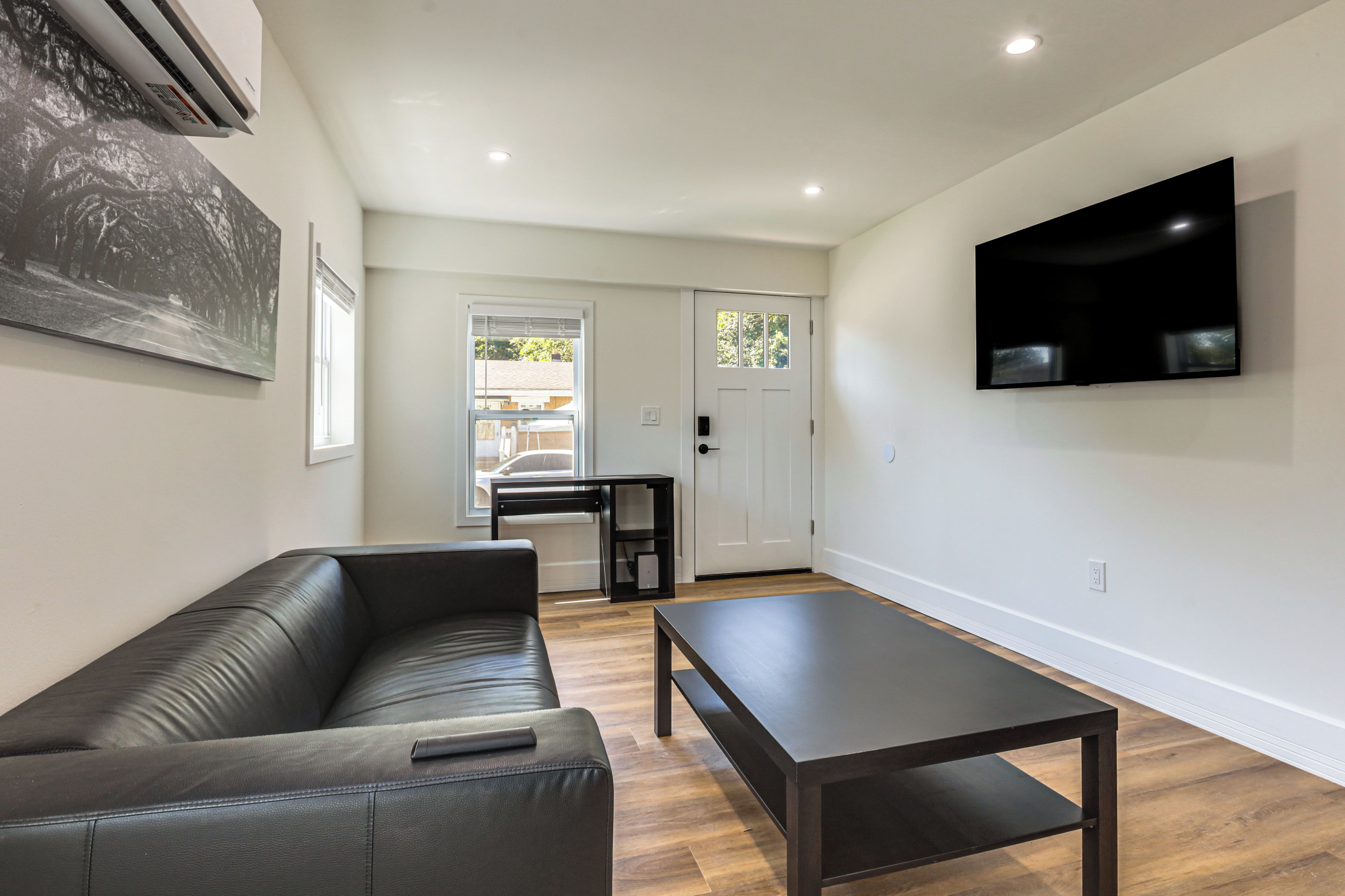 A modern living room with a leather sofa, a dark coffee table, and a flat-screen TV mounted on the wall.