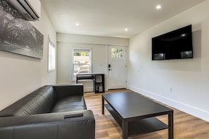 A modern living room with a leather sofa, a dark coffee table, and a flat-screen TV mounted on the wall.