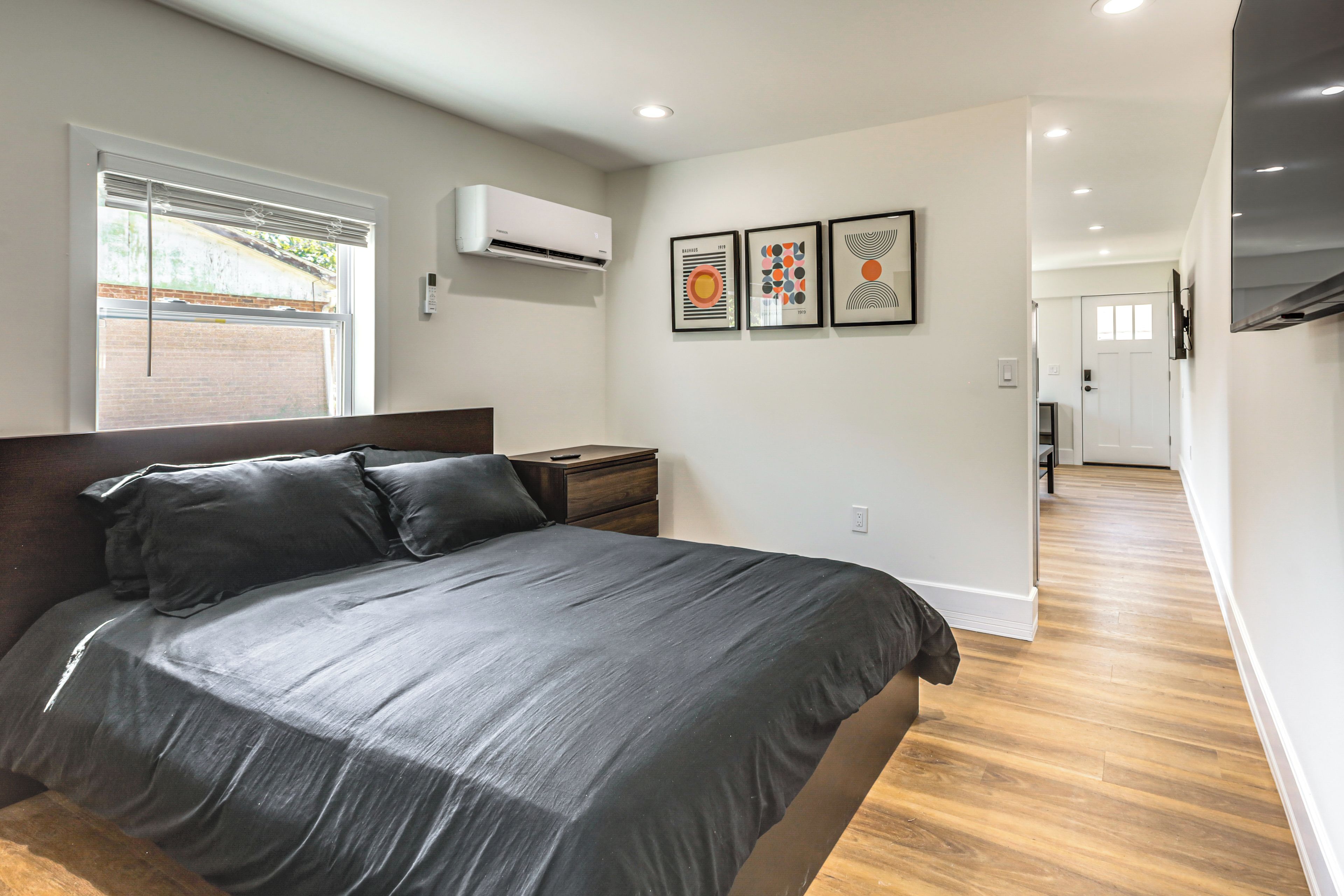 A bedroom with a bed, a nightstand, a wall-mounted air conditioner, and three framed artworks.