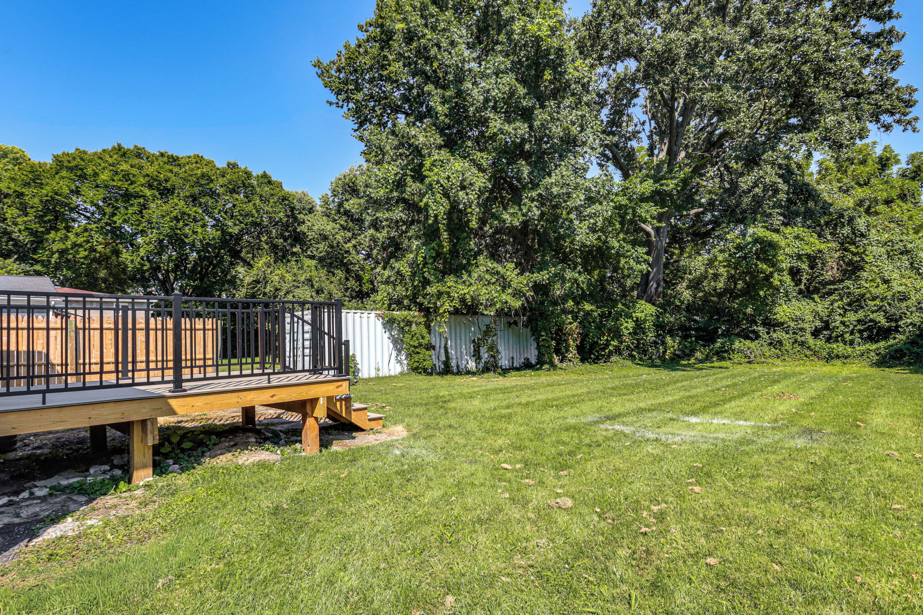 A deck with a railing overlooking a grassy yard with trees.
