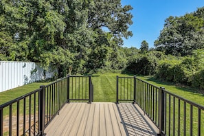A wooden deck with black railings leading to a grassy area surrounded by trees.