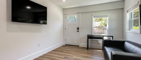 A modern living room with a flat-screen TV mounted on the wall, a black leather sofa, and a wooden floor.