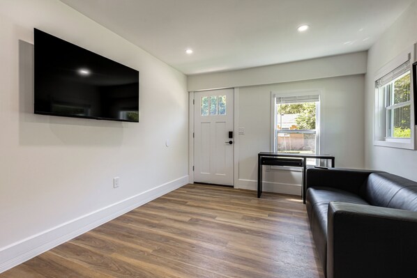 A modern living room with a flat-screen TV mounted on the wall, a black leather sofa, and a wooden floor. - Modern Retreat w/ Deck & Workspace Unit A (Cincinnati)