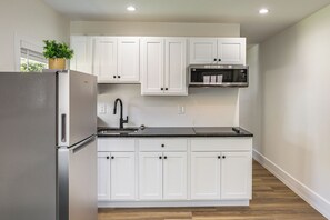 A modern kitchen with white cabinetry, a stainless steel refrigerator, a microwave, and a sink. - Modern Retreat w/ Deck & Workspace Unit A (Cincinnati)
