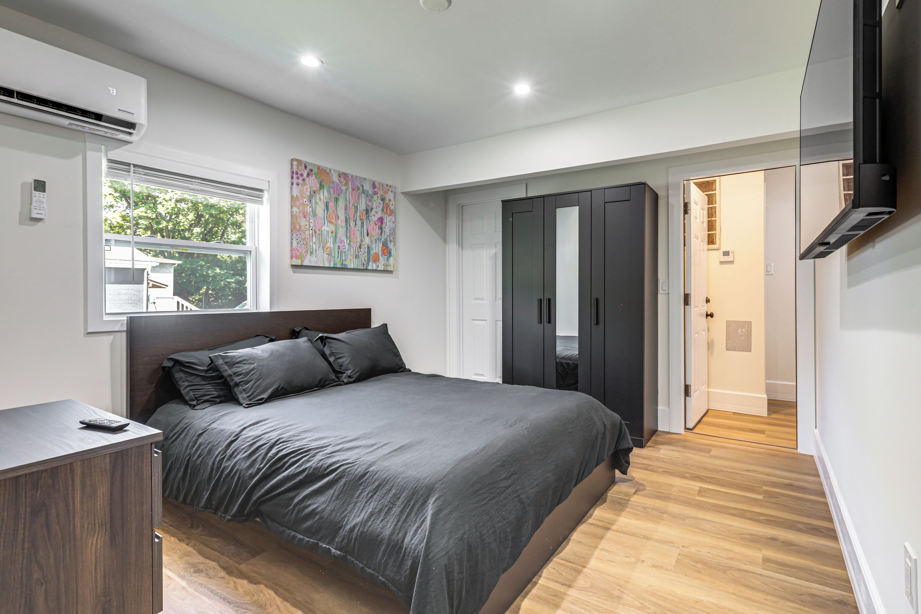 A modern bedroom with a large bed, wardrobe, and a TV mounted on the wall.