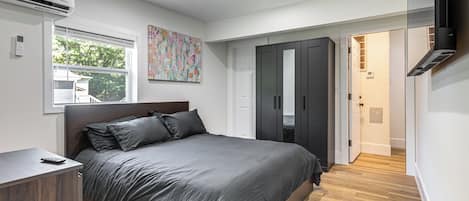 A modern bedroom with a large bed, wardrobe, and a TV mounted on the wall.