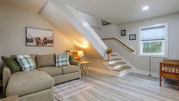 A living room with a sofa, a rug, a lamp, a picture on the wall, and a staircase.