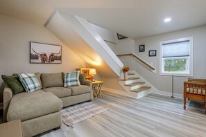 Una sala de estar con un sofá, una lámpara, un cuadro en la pared, una escalera y una ventana.