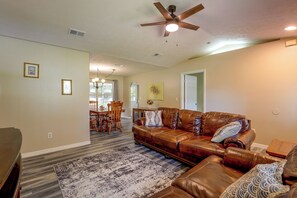 A living room with a brown leather sofa, a patterned rug, and a ceiling fan. - Near World Equestrian Ctr: Ocala Home w/ Yard (Ocala)